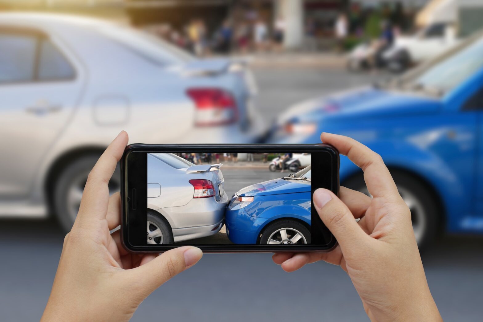 Close up of hand holding a smartphone taking photo of a car accident at the scene