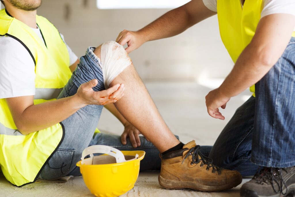 Construction worker in yellow vest checking on coworker with injured knee
