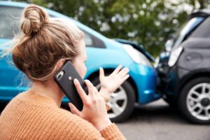 Woman on phone looking at two vehicles that recently collided.
